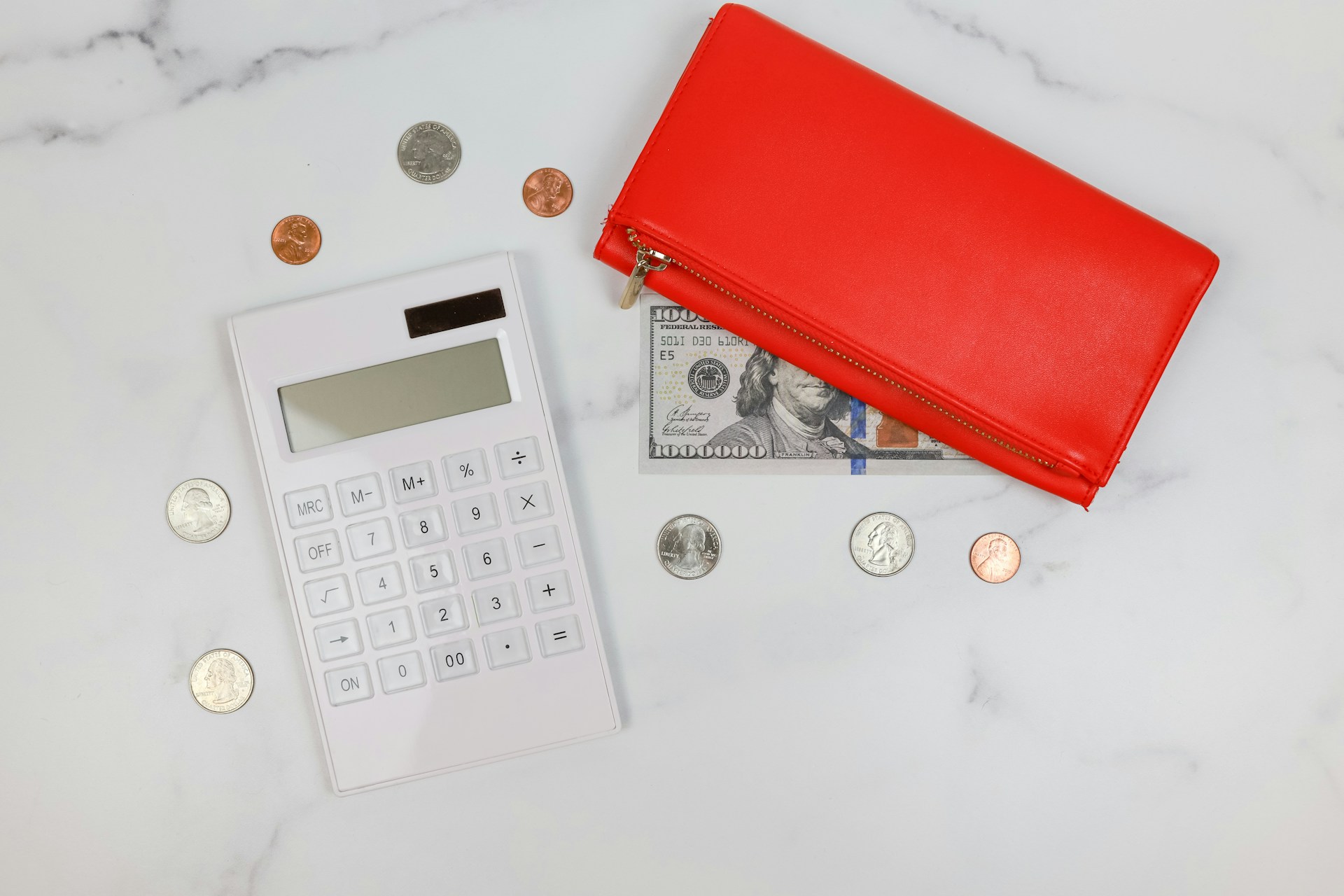 A red wallet next to dollar bills and coins on a marble countertop.