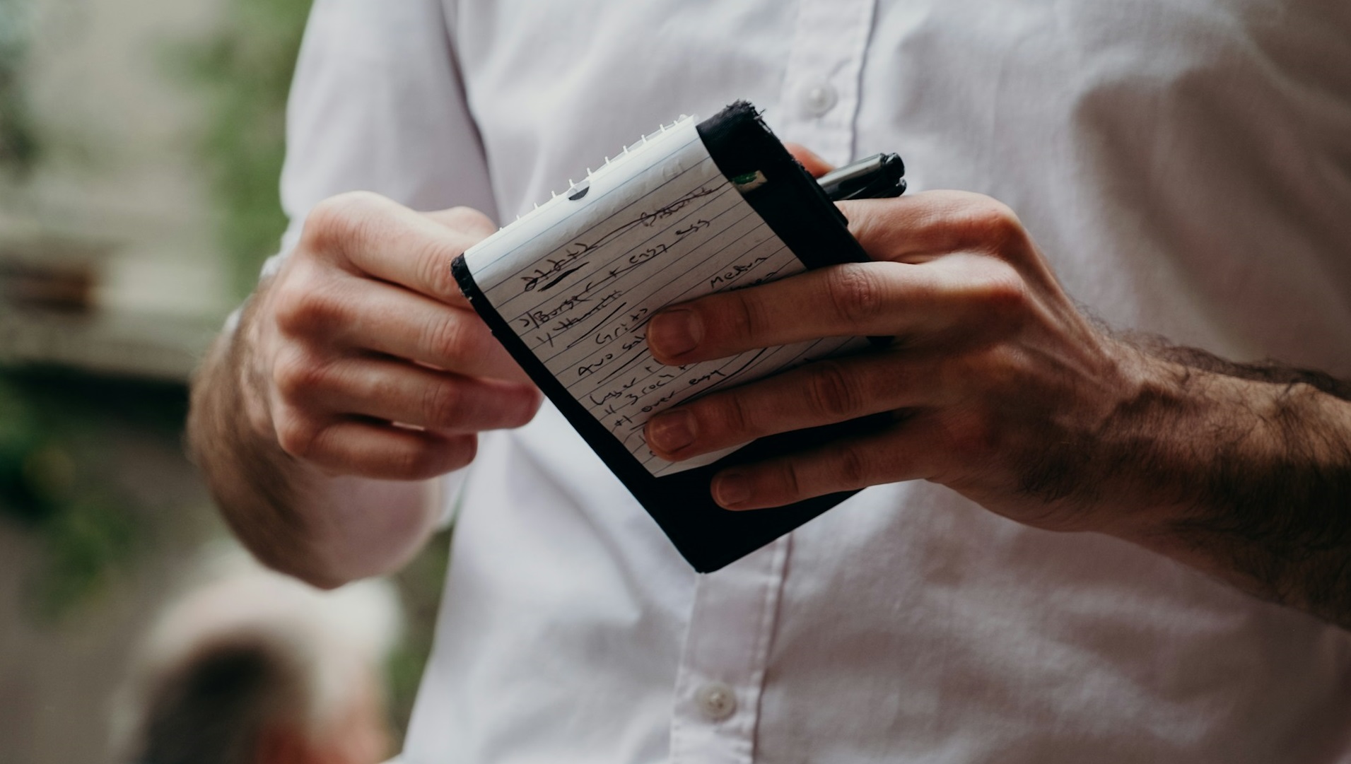 A man in a white shirt holding a booklet and a pen.