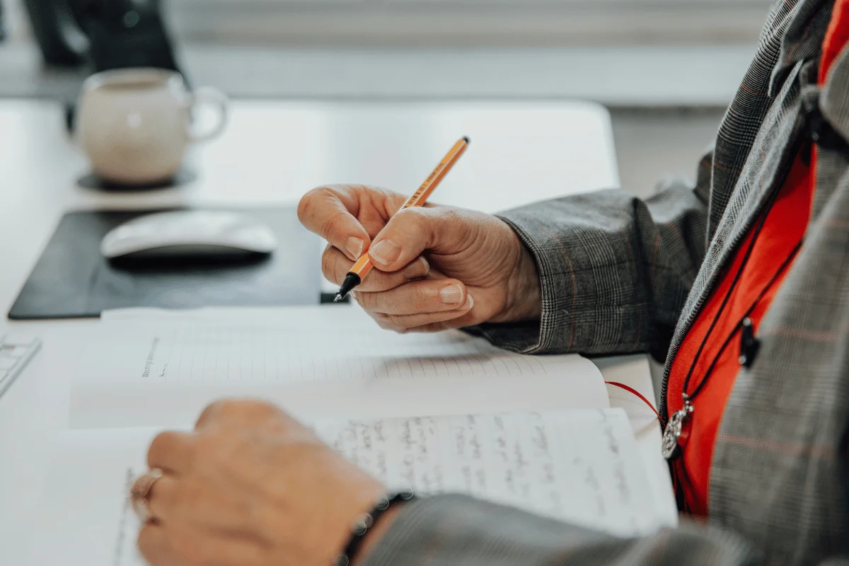Close-up of a person writing notes in a notebook on a desk.