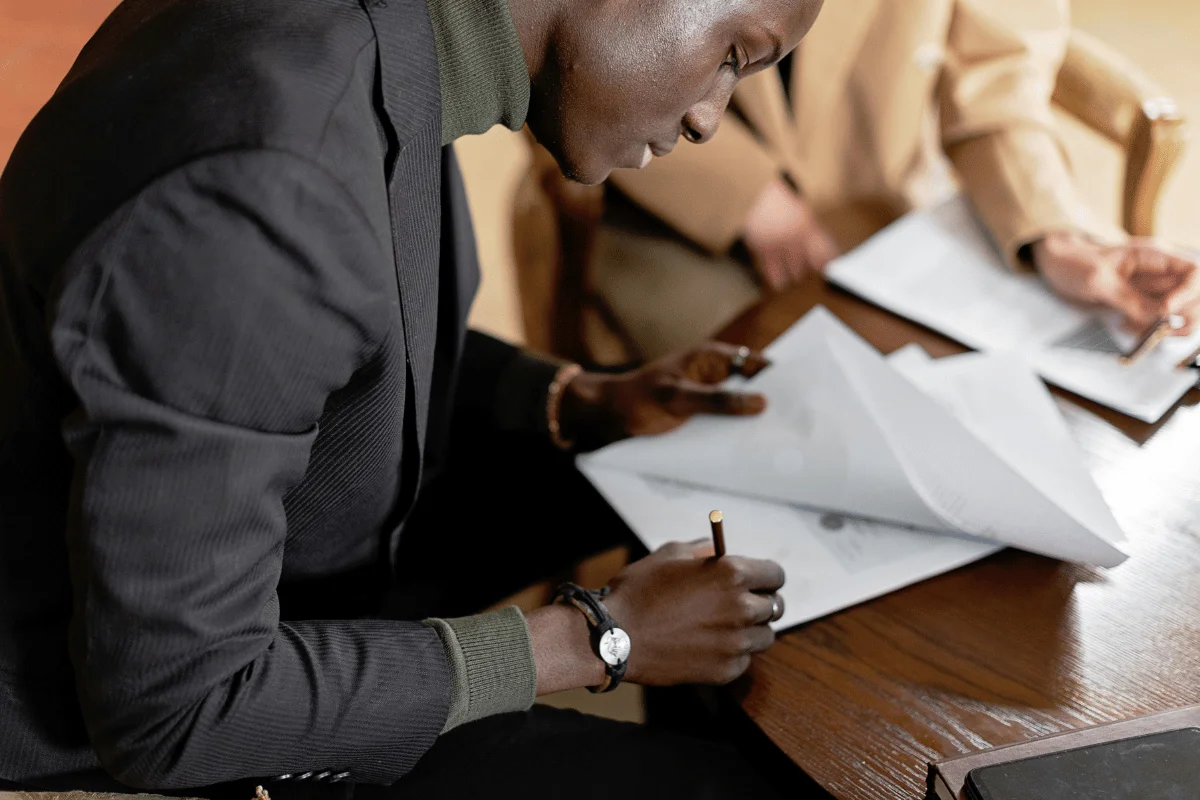 Businessman signing documents at a wooden desk in a formal setting.