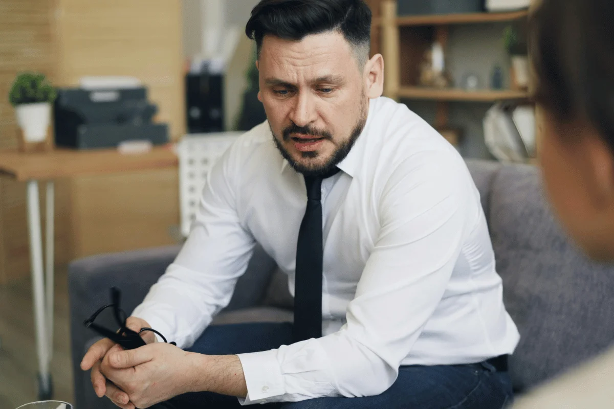 Professional man in a white shirt and tie holding glasses during a serious discussion.