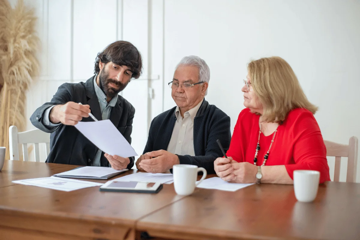 Three professionals reviewing documents at a wooden table with coffee mugs.