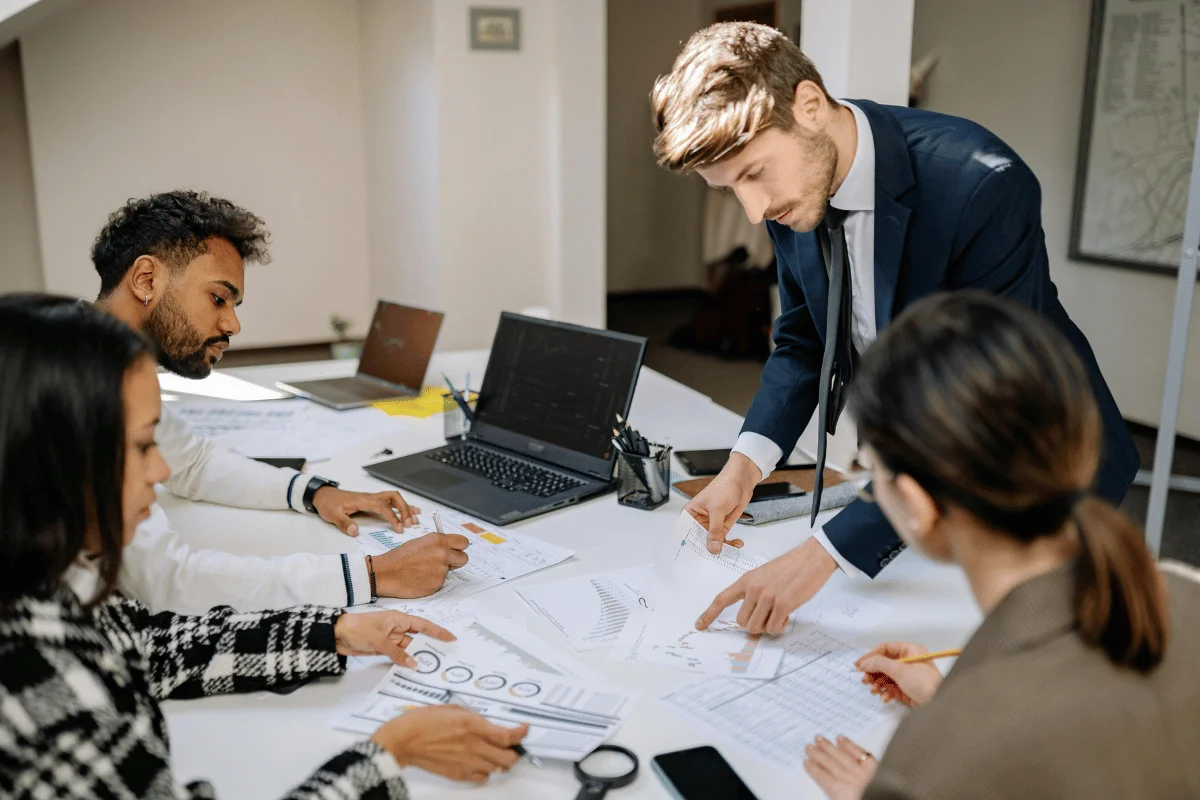 Professionals around a table with documents and laptops, engaged in a discussion.