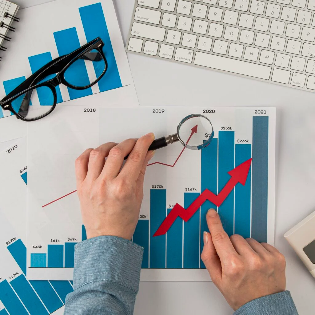 A man holding a magnifying glass over a bar graph and pointing to an upward trend.