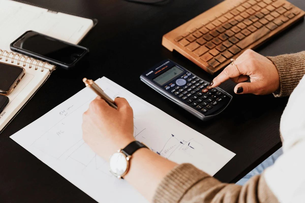 Person using a calculator while writing notes at a desk.
