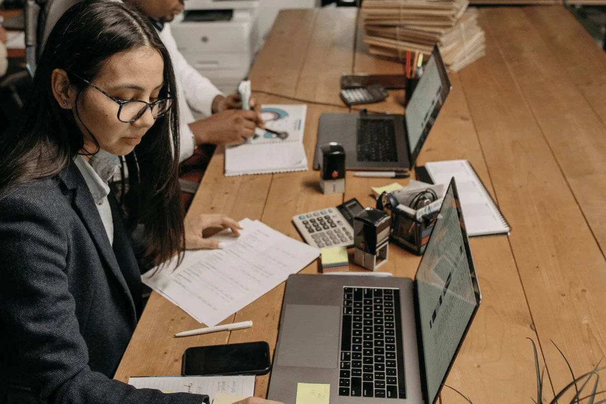 Businesswoman working on financial documents at a wooden desk with a laptop and calculator.