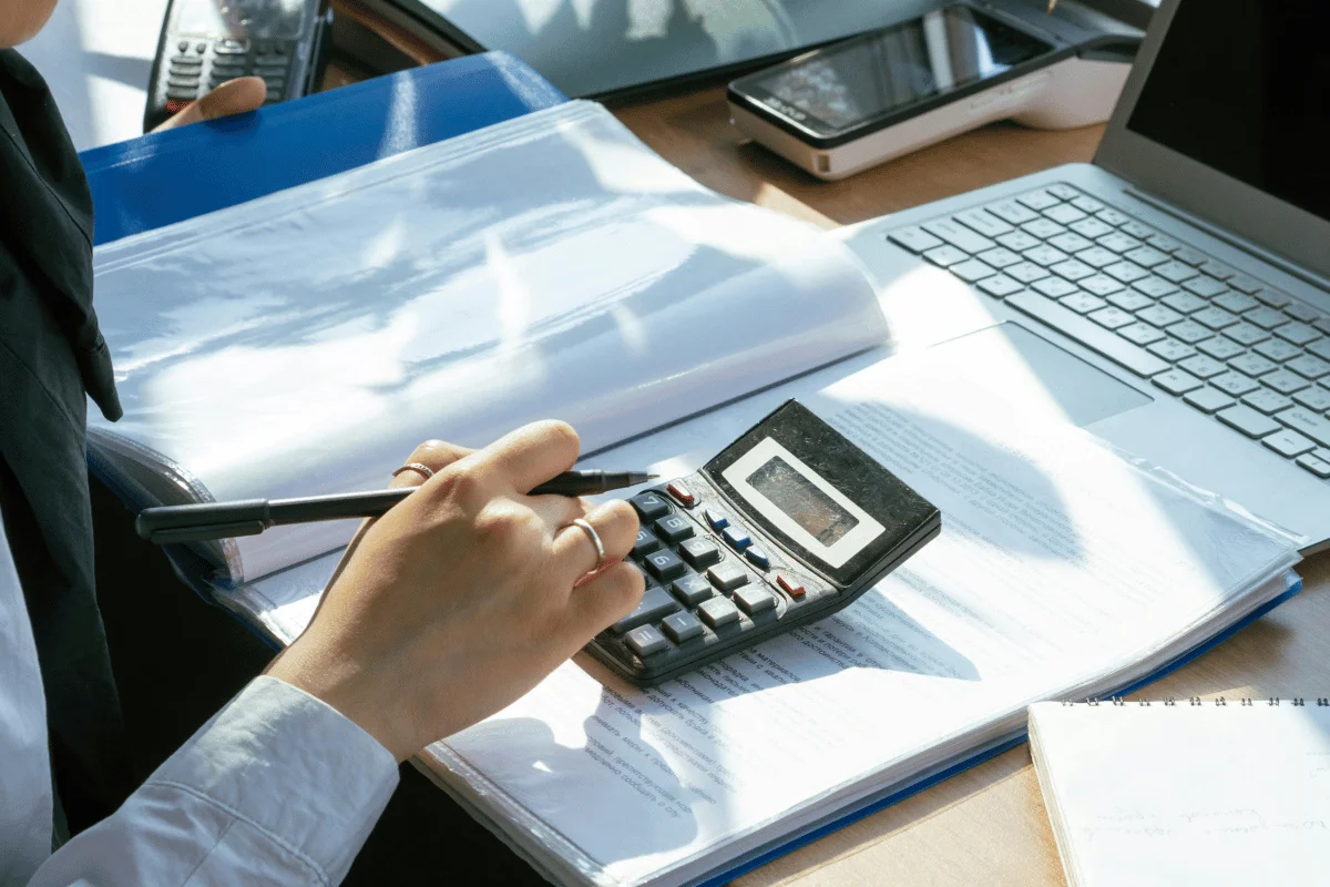 Business person using a calculator while reviewing financial documents at a desk.