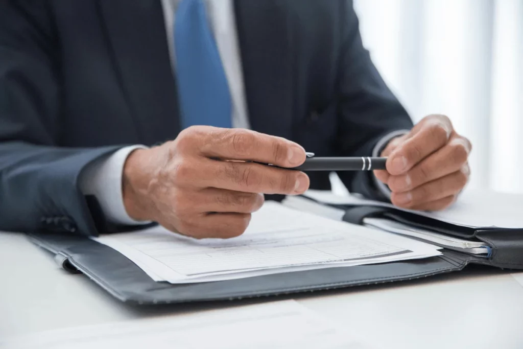 A close-up of a businessman's hands holding a pen over documents on a desk.