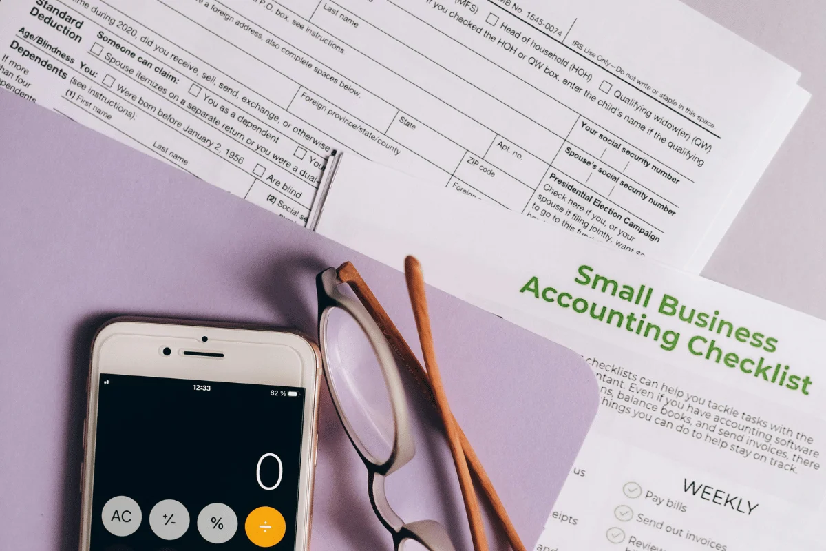 Small business accounting checklist alongside tax documents and a smartphone calculator.