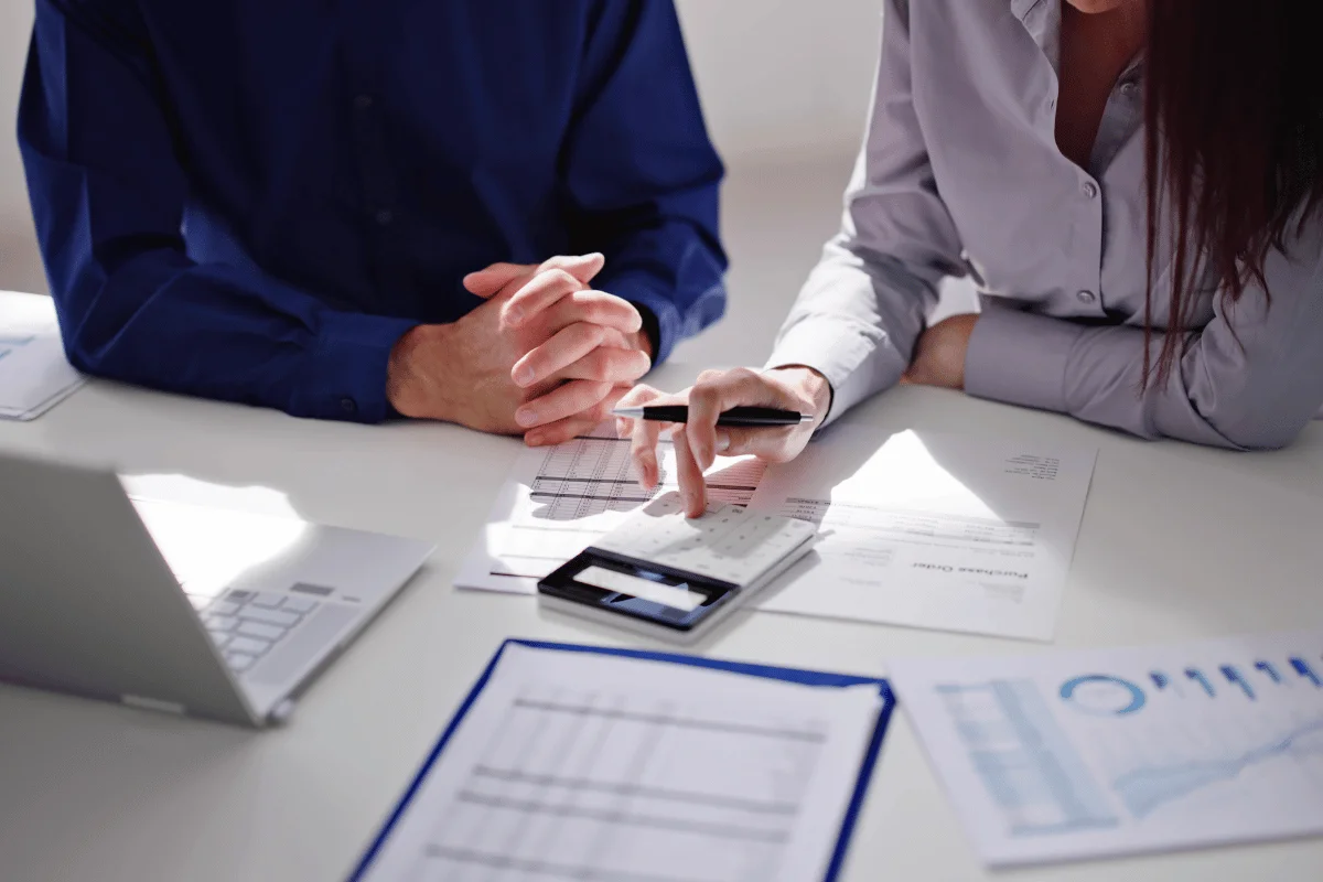 Two business professionals analyzing financial reports at a desk with a calculator.