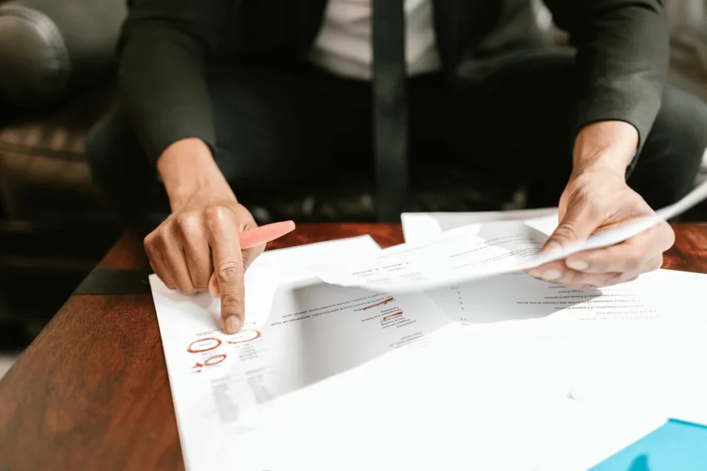Businessman analyzing paperwork with red pen markings highlighting important data.