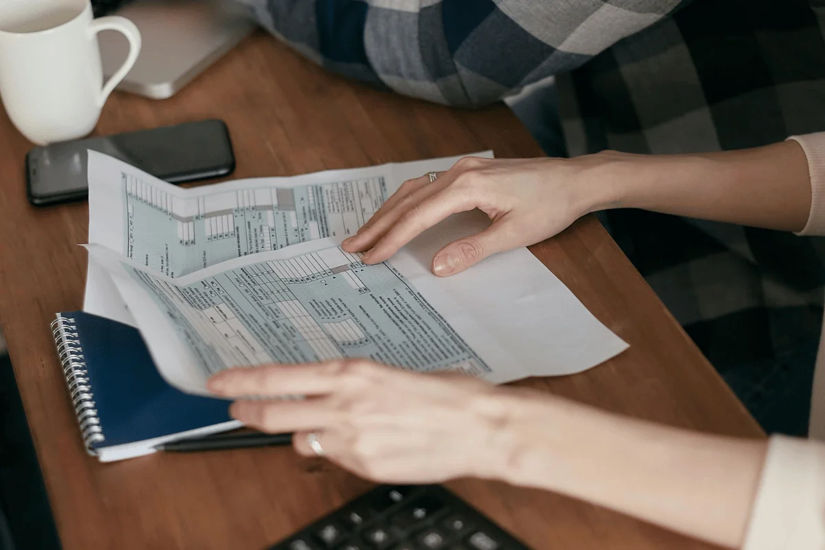 Person reviewing financial documents at a wooden desk with a cup of coffee.
