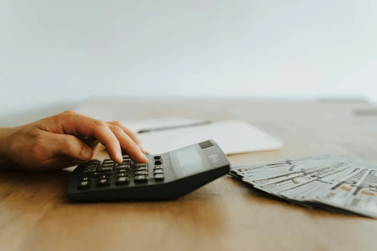 Close-up of a hand pressing calculator buttons with cash and a notebook in the background, symbolizing financial analysis.