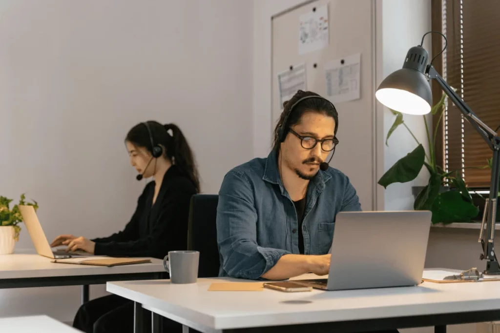 Male customer service agent with a headset working on a laptop in a modern office.