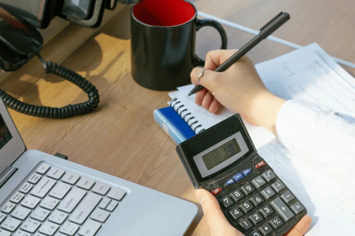 Person using a calculator while writing notes on a spiral notebook.