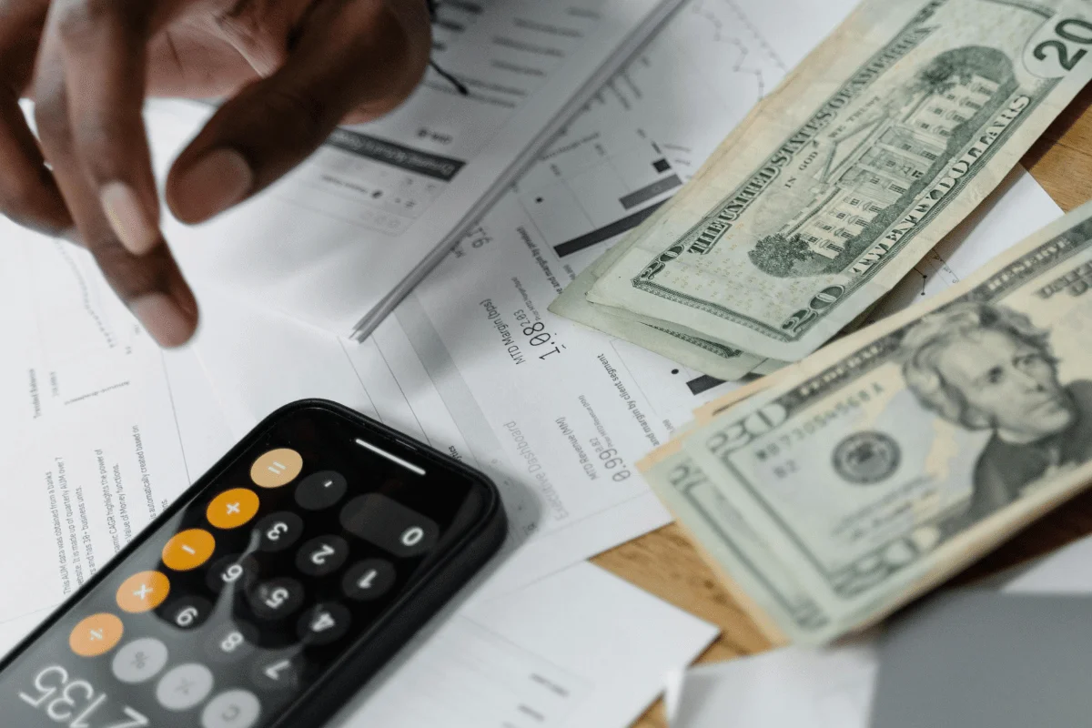 Financial planning with a smartphone calculator, cash, and financial reports on a desk.