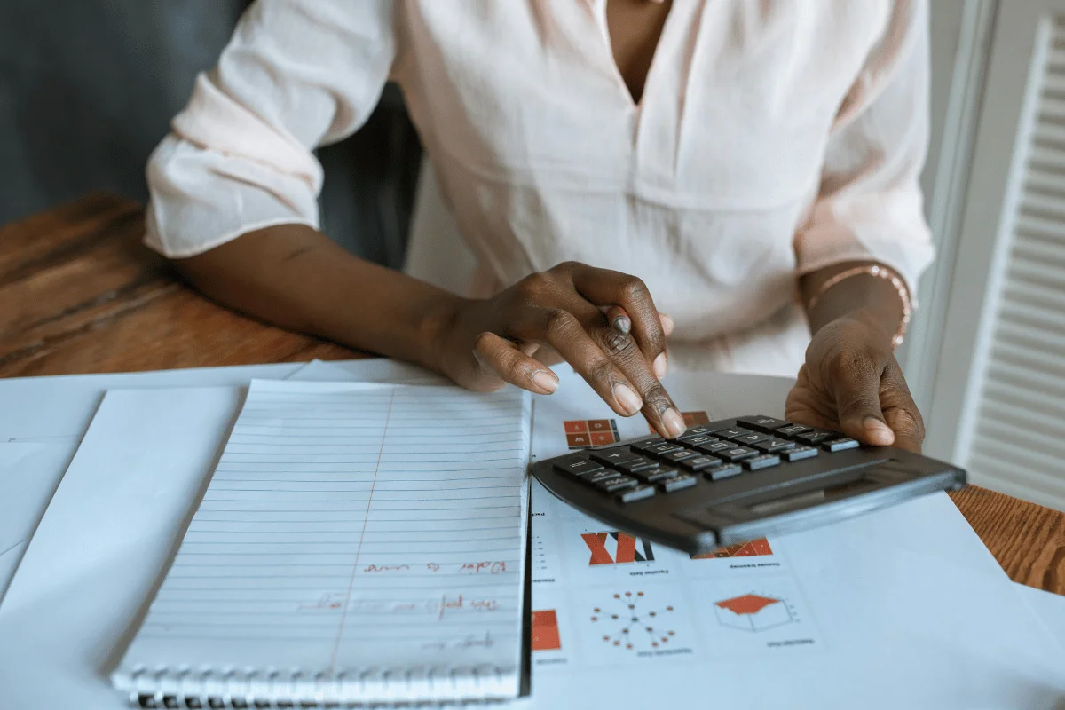 A person calculates data using a digital calculator, surrounded by papers and graphs on a wooden table.