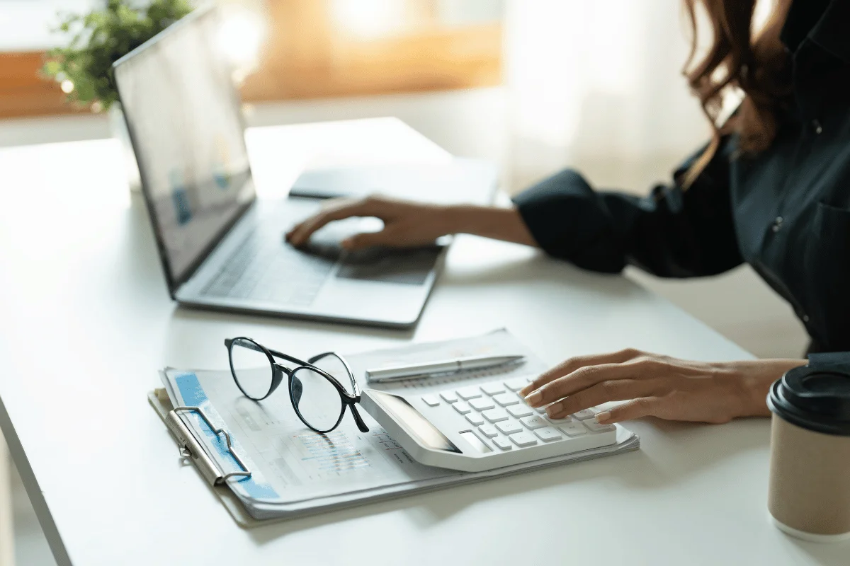 Businesswoman using a calculator and laptop while working with financial charts.