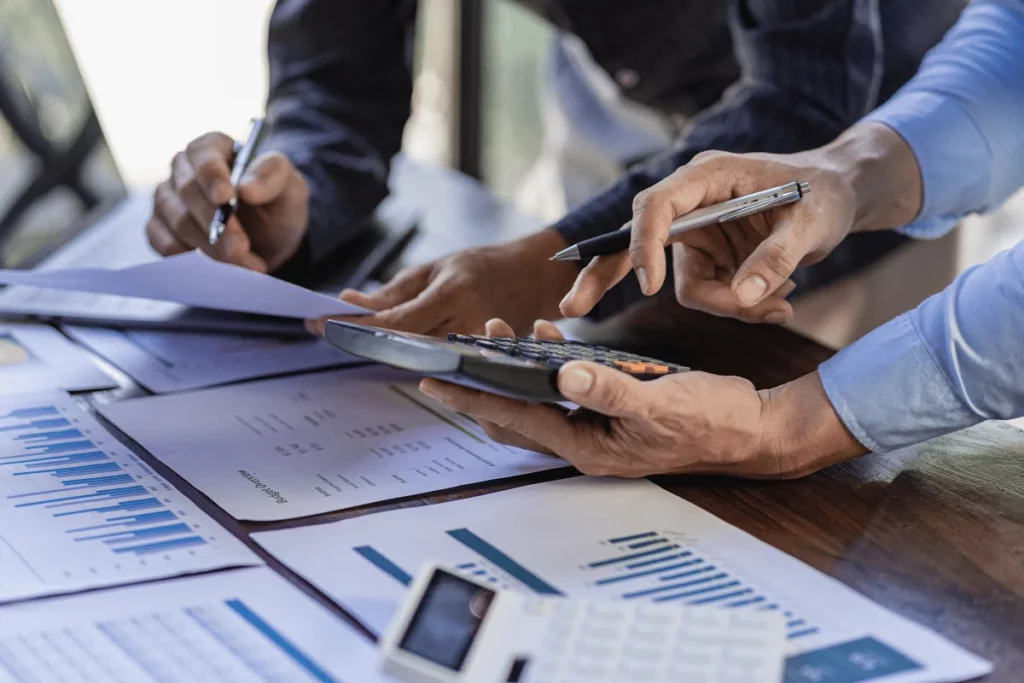 Hands of two professionals discussing data with a calculator and financial charts on the table.