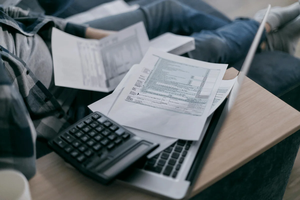 Tax forms and a calculator resting on a laptop on a wooden desk.