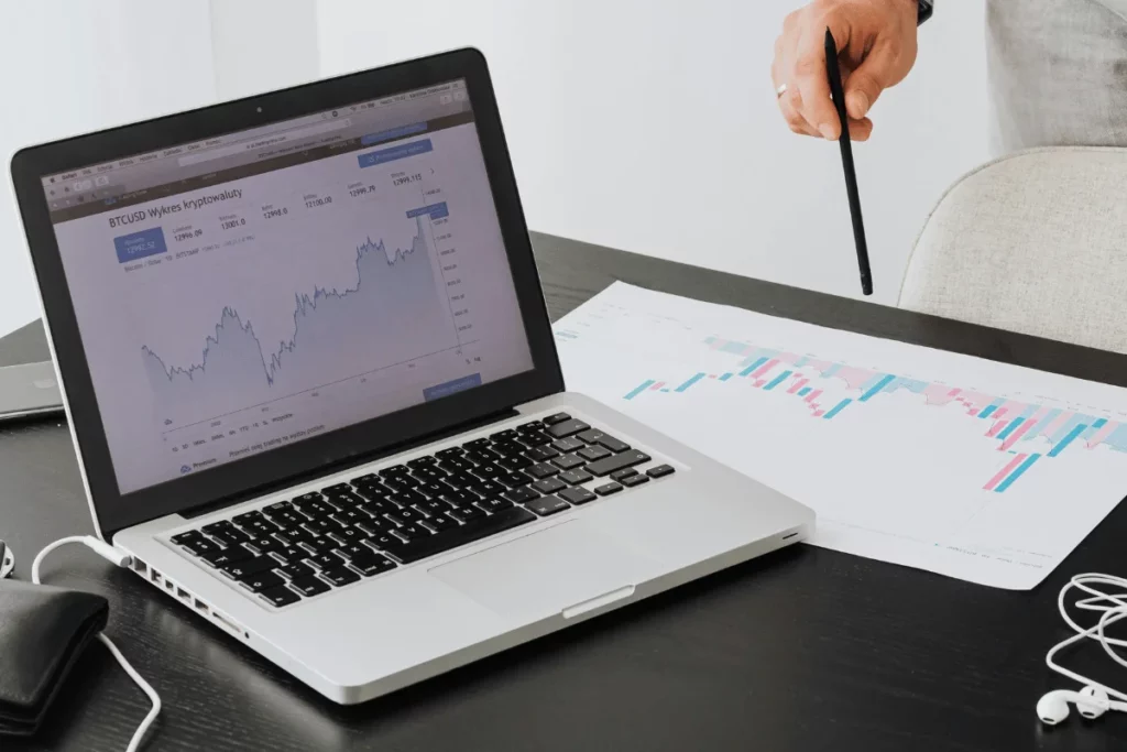 Close-up of a laptop showing a BTC/USD chart alongside financial reports.