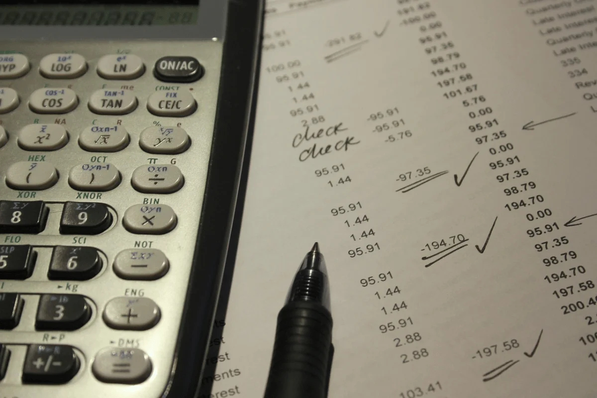 A close-up shot of a calculator next to an accounting sheet with checkmarks and crossed-out entries.