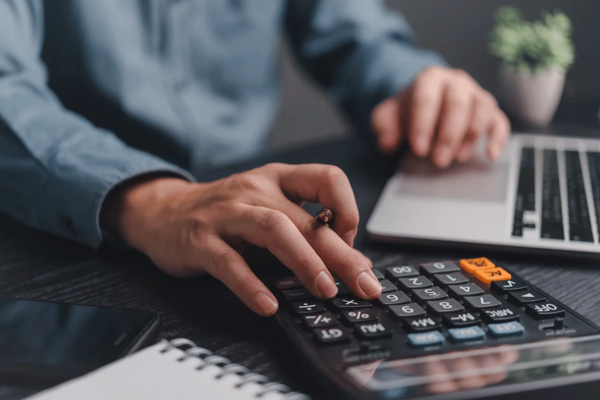 A professional using a calculator and a laptop for financial planning on a desk.