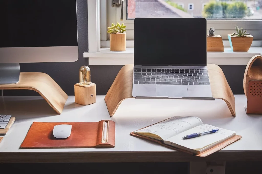 A laptop on a desk beside a book and a pen, creating a workspace for study or work.