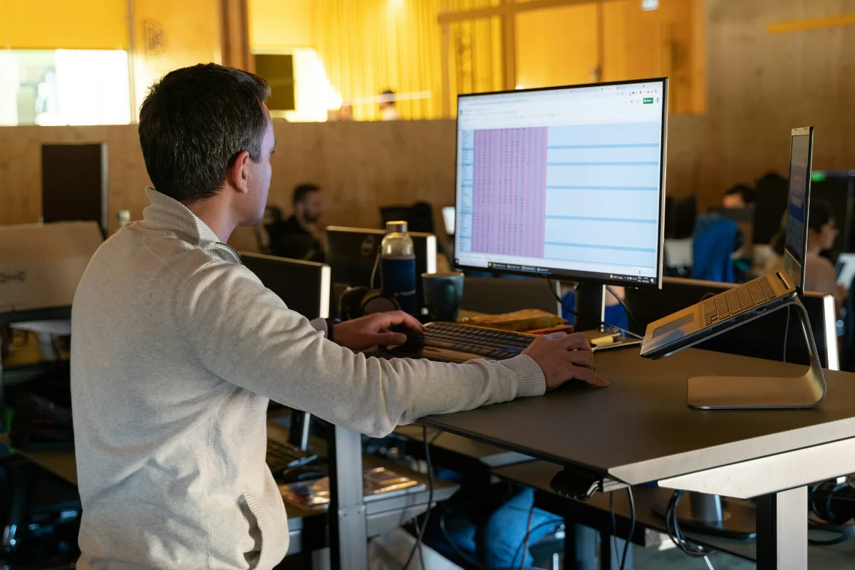 Professional working at a standing desk reviewing spreadsheet data on a large monitor in a modern office.