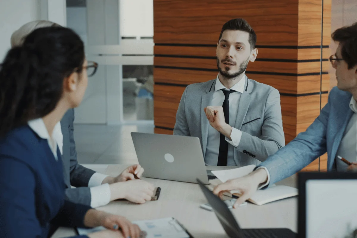 Business professionals discussing strategy during a meeting with laptops and documents in a modern office.