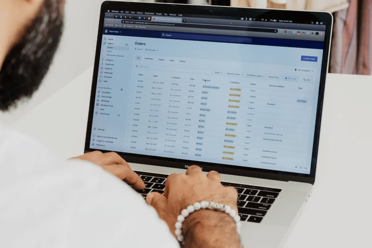 A person types on a laptop displaying an order management screen. The scene conveys focus and productivity, with order data organized in columns.