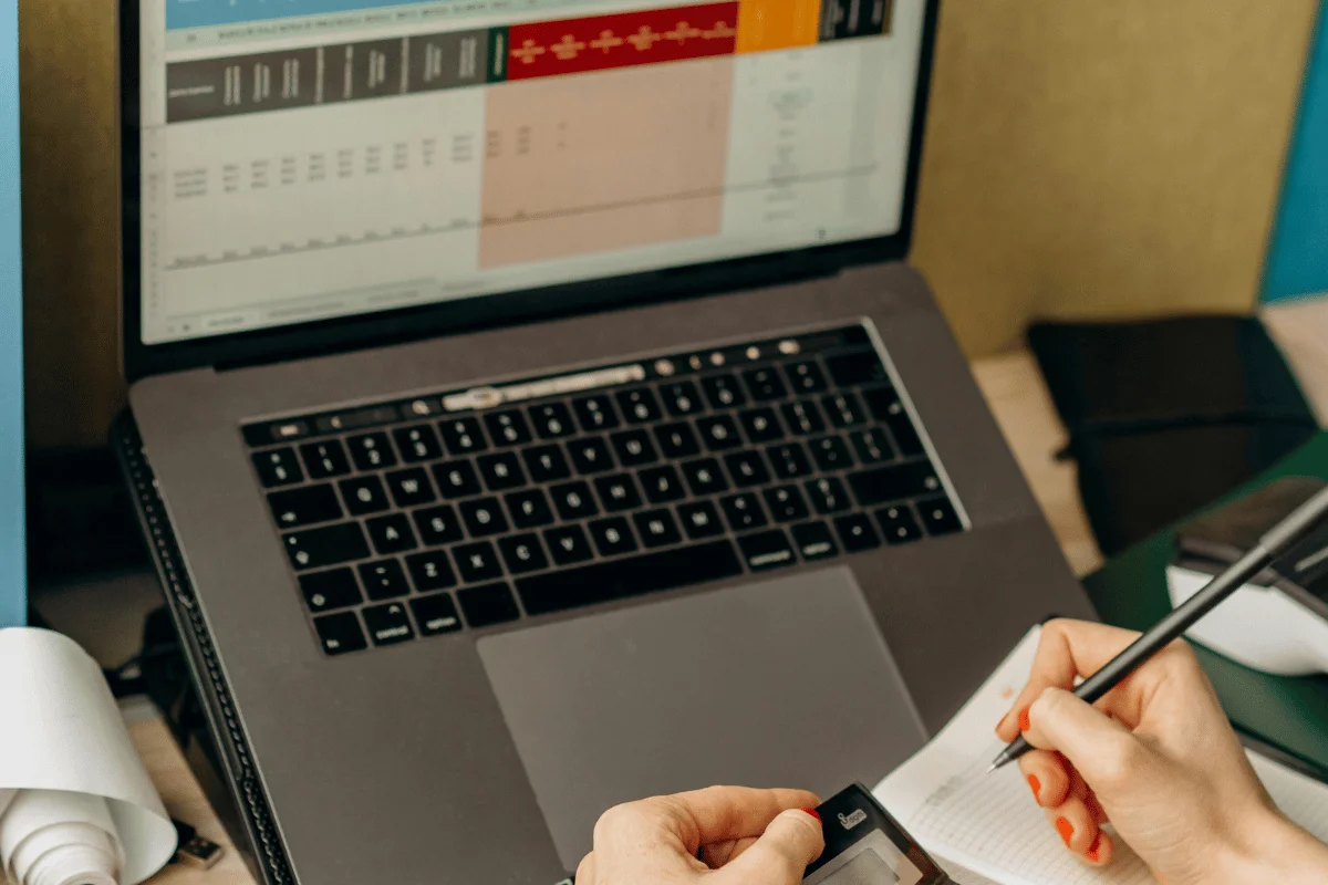 Business professional working on financial reports using a laptop and notepad.