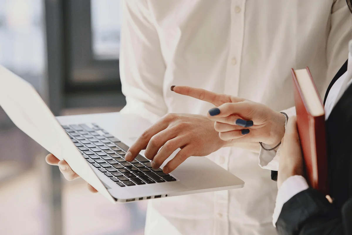 Two professionals reviewing a laptop together while one points at the screen during an office discussion.