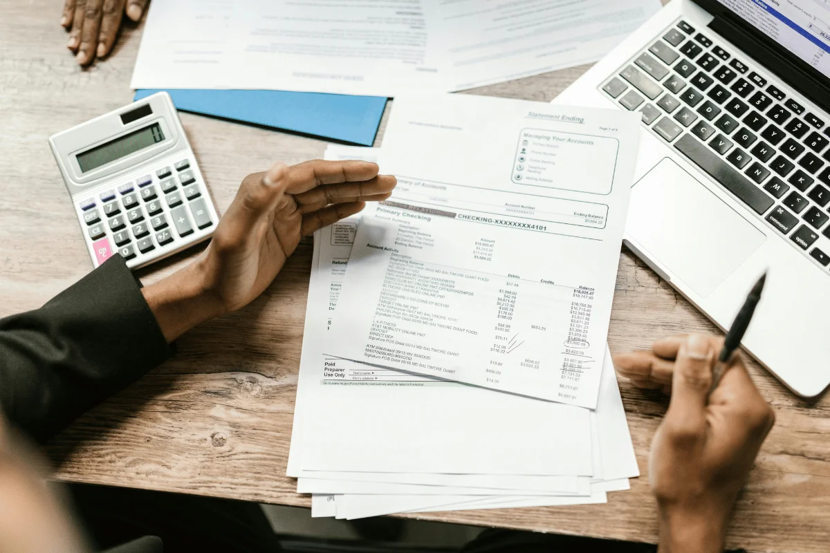 Close-up of financial documents, calculator, and laptop on a wooden desk.