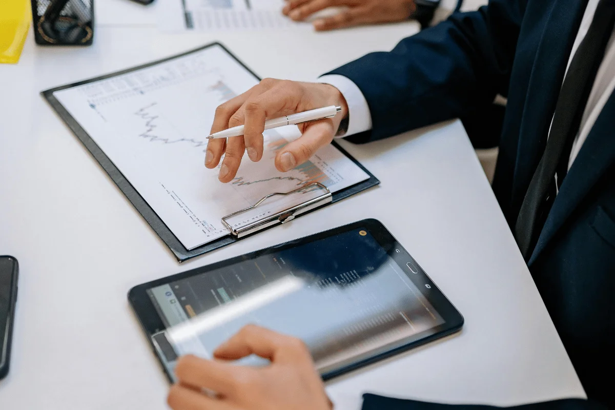 Business professional reviewing charts on a clipboard while using a tablet during an office meeting.