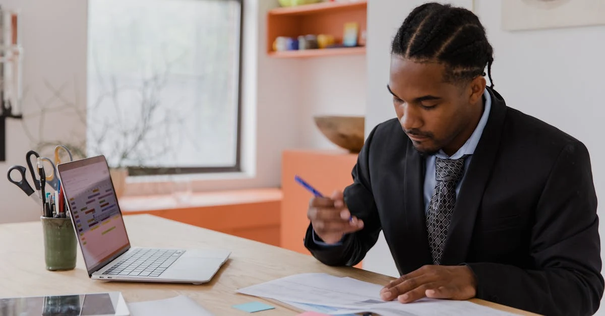 Professional man reviewing small business tax deductions documents at desk with laptop and organized workspace.