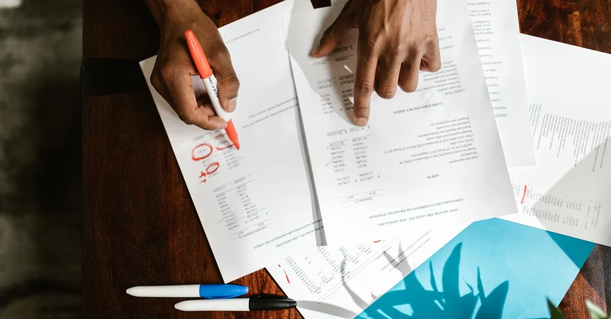 Person reviewing financial documents and chart of accounts small business statements on wooden desk with pen.