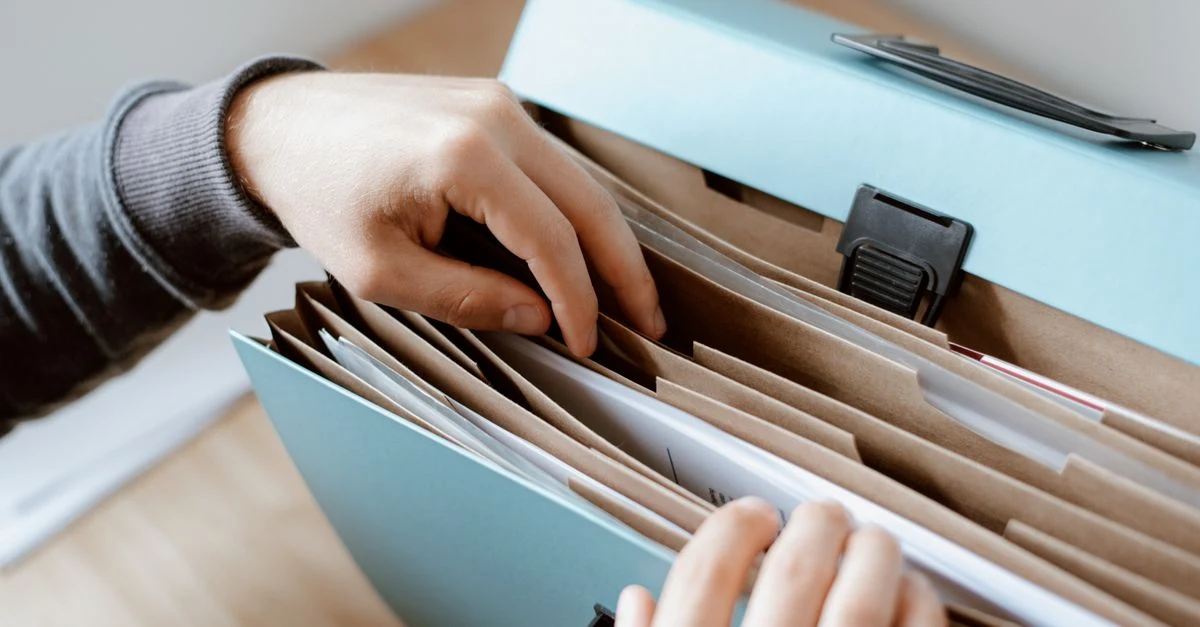 Hands organizing labeled file folders in accordion organizer for small business tax preparation documentation.