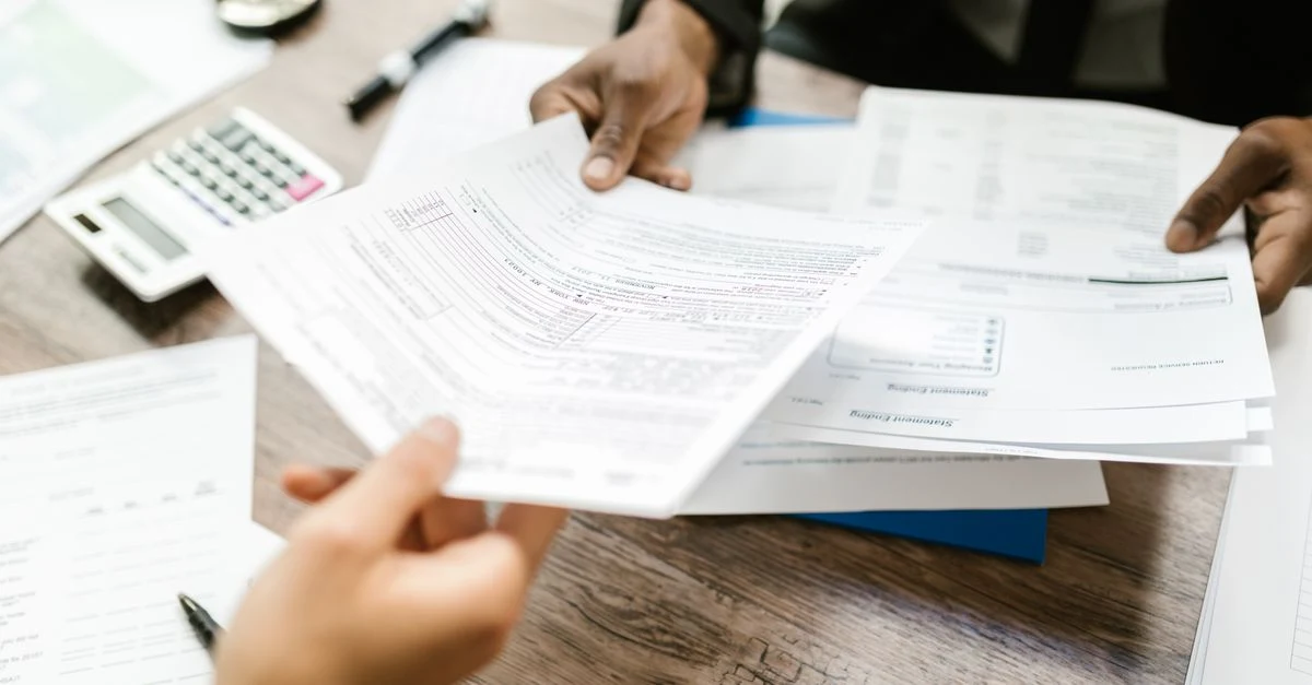 Two professionals reviewing small business tax preparation documents and financial charts at wooden desk with calculator.