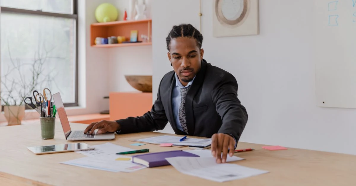 Professional man reviewing owners equity statement documents at wooden desk with laptop and colored papers.