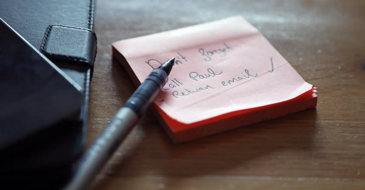 Pen writing notes on pink sticky note next to wallet for small business tax preparation checklist organization.