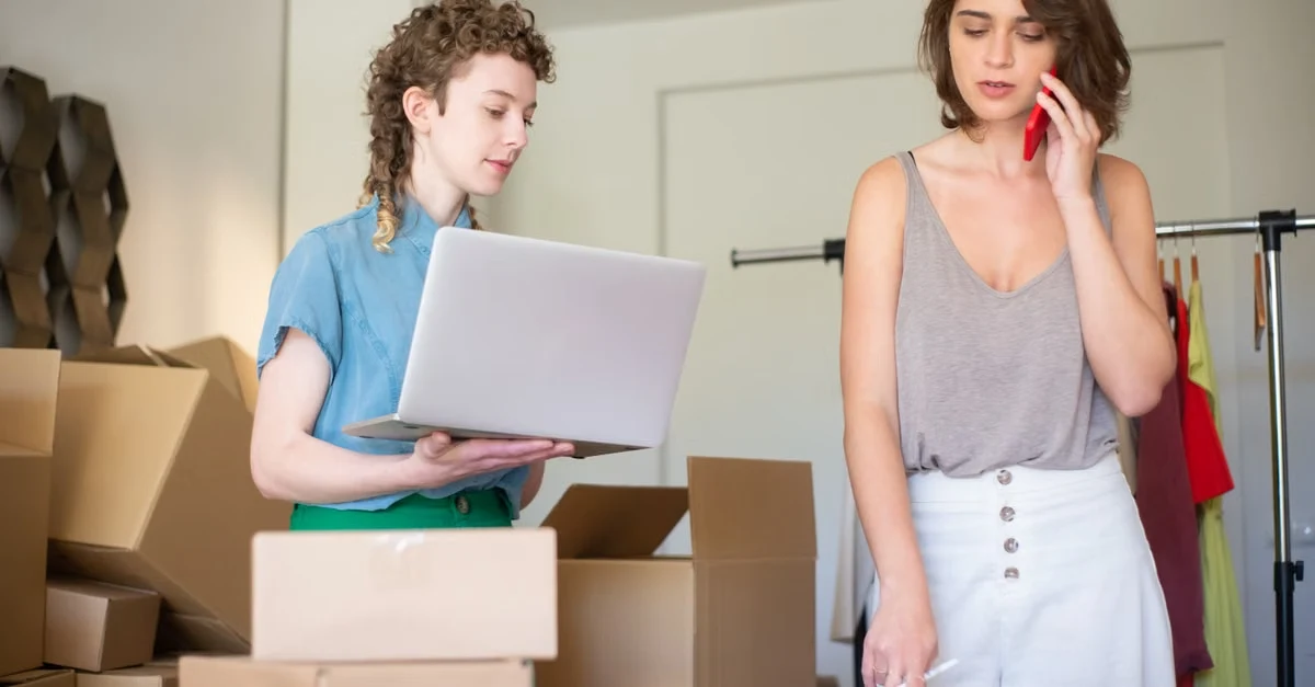 Two people in modern office organizing cardboard boxes and checking laptop for year end tax planning deadline.
