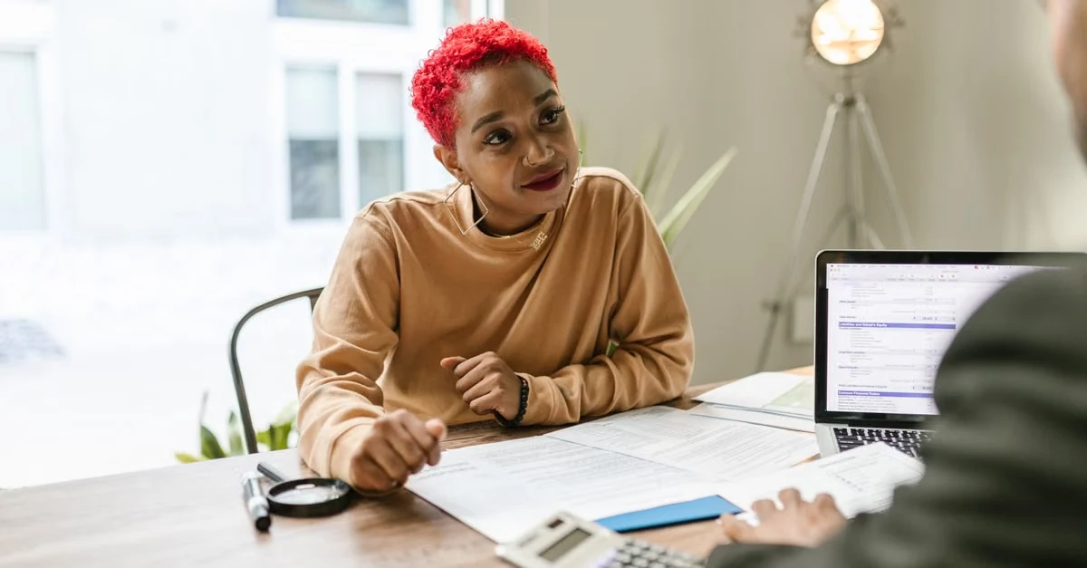 Woman with pink hair discusses tax planning business owners strategy at desk with laptop and financial documents.