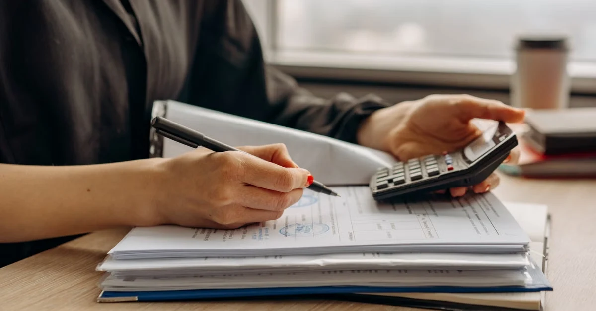 Person doing year end tax planning with calculator, pen, and financial documents at desk.